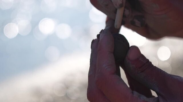 Crafting, hands, artisan shaping small clay object with tool outdoors under bright sunlight