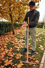 Man cleaning garden from fallen autumn leaves.