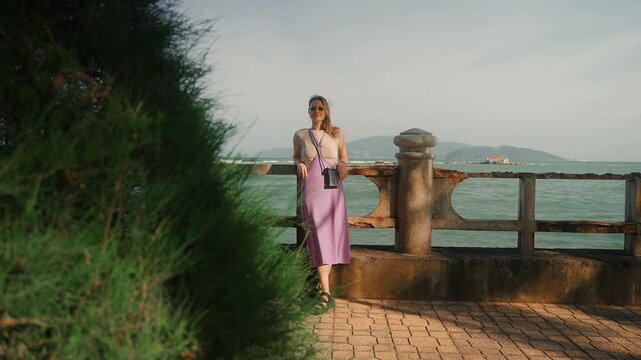 young woman in purple dress stands on a parapet and looks into the distance. A blonde girl looks into the distance at an island.
