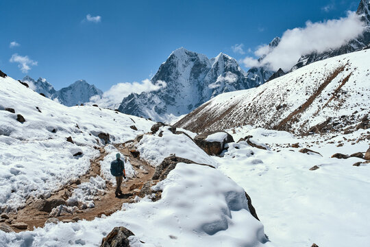 Alone backpacker confidently walks along mountain trail Everest Base Camp in Nepal with majestic snow-capped peaks of Himalayas in background.