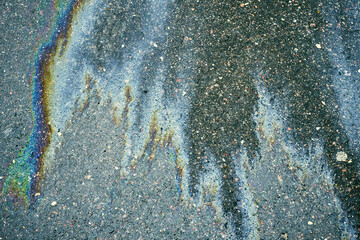 Oil or gasoline spill creating colorful iridescent reflections on wet asphalt surface. Showing pollution and environmental impact