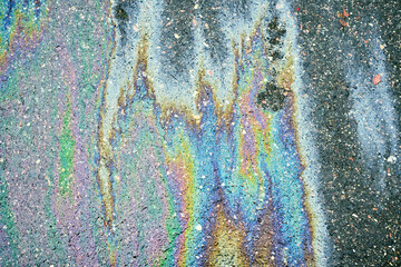 Oil slick on an asphalt road creating an iridescent rainbow spectrum of colors and reflecting light, representing pollution and environmental issues