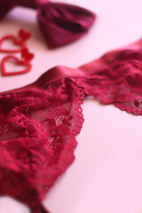 Red lace bralette, hairbow, heart shaped earrings, golden ring, red lipstick and nail polish on pink background. Coquettish accessories for Valentine's day. Selective focus.
