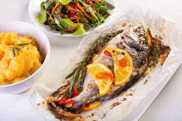 Whole baked dorado fish with orange slices, chili and orange puree, elegant seafood dinner plate.