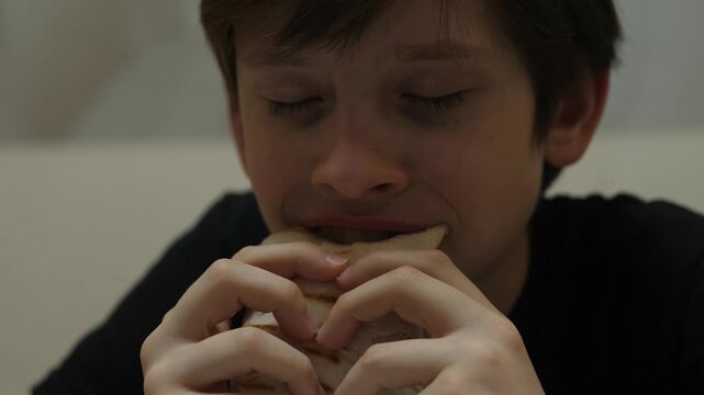Close-up of a teenage boy biting and chewing an appetizing shawarma with pleasure. The child enjoys the taste of fast food in a home setting