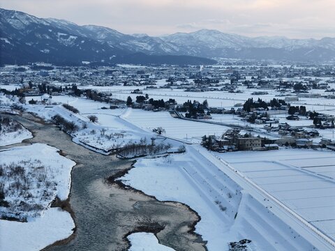 A snowy landscape with a river and mountains in the background. The city is in the distance