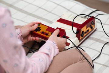 Little girl playing a vintage game console on the bed. Retro style, nostalgia for the 80s and 90s.