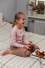 Little girl playing a retro game console while sitting on a bed. Vertical orientation.