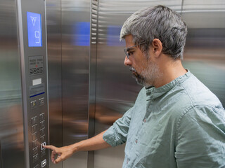 Man pushing an elevator button, selecting a destination inside a lift for routine movement between different levels © Nuria Gonzalez Sanch