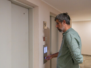 Fototapeta premium Man standing in a corridor, pressing call button for an elevator. Concept of transportation, accessibility, and waiting