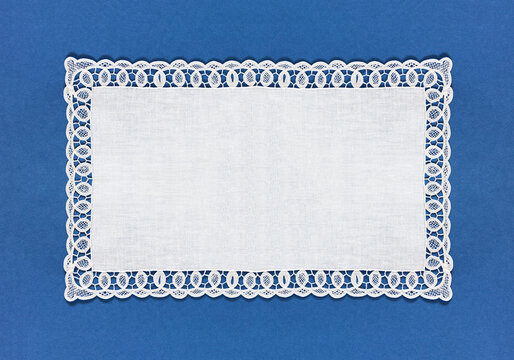 A rectangular white tablecloth with an openwork lace border on a blue background. Empty space for text. Close-up, top view, copy space, flat lay, collage, banner, mock up, blank