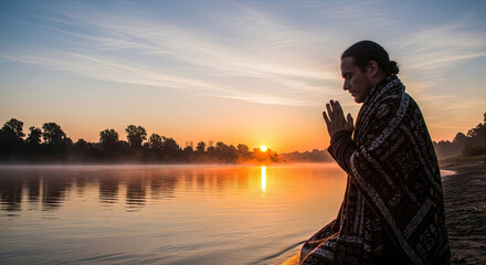 Fototapeta premium Person meditating by a river during sunset with folded hands.