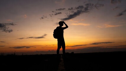 Fototapeta premium Silhouette of young male hiker overlooking dramatic sunset sky.