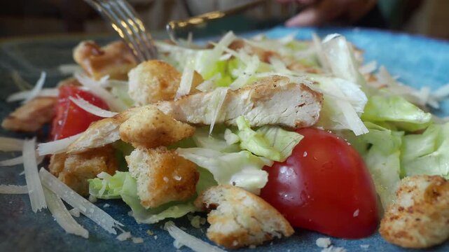Close up footage of caesar salad with chicken and croutons being eaten with fork and knife