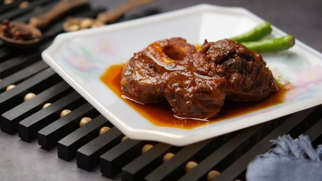 Traditional slow cooked beef osso buco stew served on white plate with green chili garnishment cinematic food footage