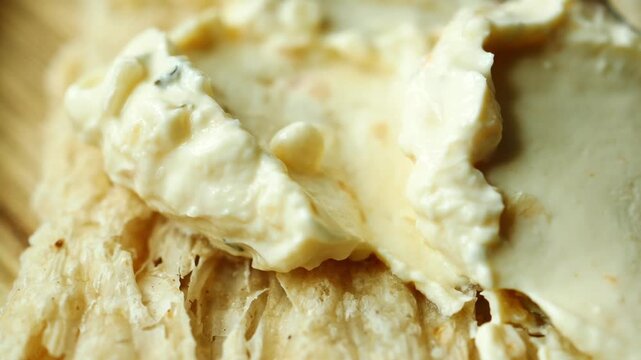 Close up slow motion shot of creamy homemade cheese being spread on flatbread pita bread on wooden background