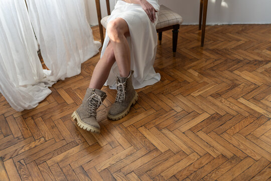 Cozy winter fashion concept. A woman sitting indoors on a vintage parquet floor, wearing warm natural beige valenki and a white dress, enjoying a calm moment in a minimalist interior.