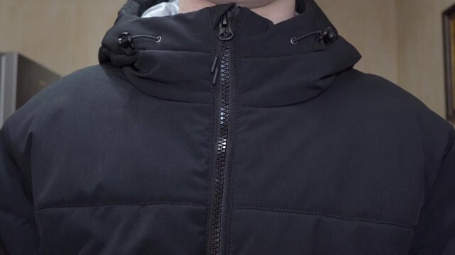 close-up of zipping up black men's down jacket, preparing for a winter walk, a man carefully zips up his warm black jacket