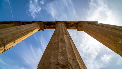 Low-angle view of ancient temple pillars reaching to sunny, cloudy sky