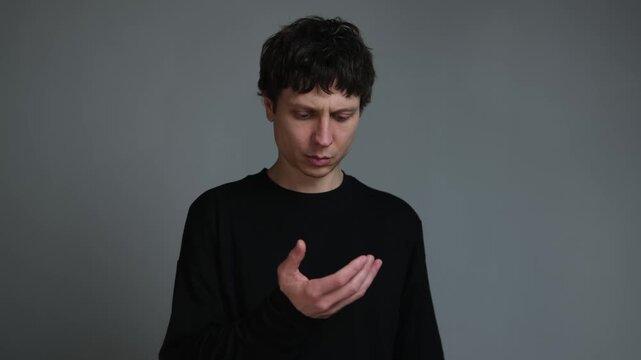 Phantom habit to reach for phone digital addiction and quiet frustration. young man staring at empty hand on neutral grey background