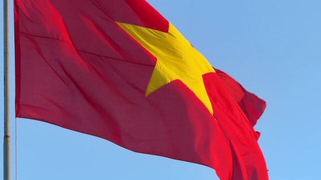Close view of Vietnam national flag in slow motion, fabric rippling clearly in the wind against a clean bright daytime sky. Civic identity.