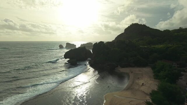 Aerial view of the beautiful Siung Beach coastline with lush green hills meeting the crashing waves, Gunungkidul Regency, Special Region of Yogyakarta, Indonesia.