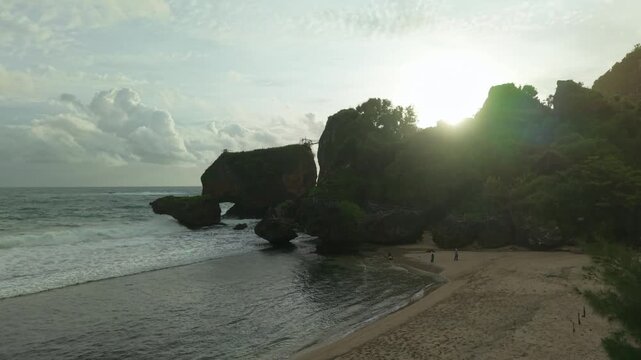 Aerial view of Siung Beach with its dramatic cliffs and crashing waves under a bright sky, presenting a tranquil yet powerful coastal scene, Gunungkidul Regency, Indonesia.