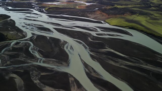Aerial view of the pale braided river system cutting through the dark Icelandic landscape, creating a stunning contrast of colors and textures, Selfoss, Iceland.