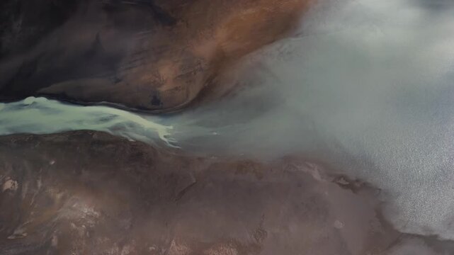 Aerial view of the river flowing into the land, contrasting the light blue hues of the water with the brown and dark land, Selfoss, Iceland.