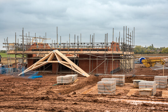 Family house construction site. Building red brick house surrounded by scaffolding with wooden roof truss. Energy-efficient homes estate development. Works on new residential properties for homebuyers