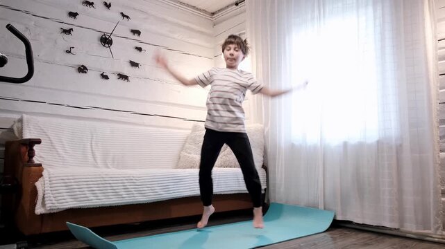 Caucasian boy doing an exercise Jumping Jacks on yoga mat at home. Children workout. Morning warmup. Child strengthening the muscles of legs, endurance and balance. Strong sporty body. HQ 4k footage.