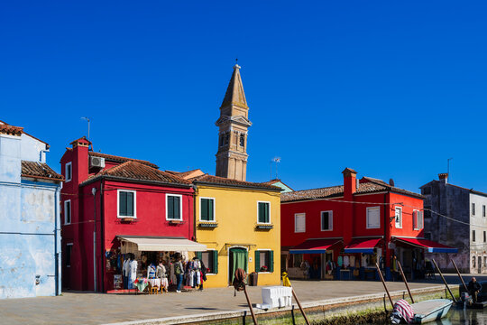 Colorful buildings with a tall bell tower under a clear blue sky in a waterside town. Burano, Venetian Lagoon, Italy