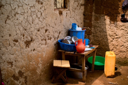 Rustic outdoor setting with clay walls, a wooden table, and household items in blue and orange.   Kigali, Rwanda