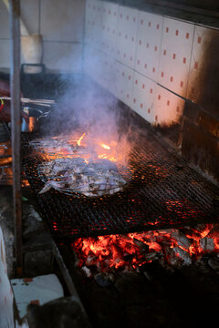 Fish grilling over a charcoal fire with smoke rising in a tiled kitchen setting. Kigali, Rwanda