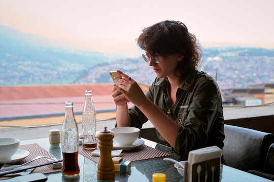 Young woman using smartphone at outdoor restaurant with cityscape view in the background. Kigali, Rwanda