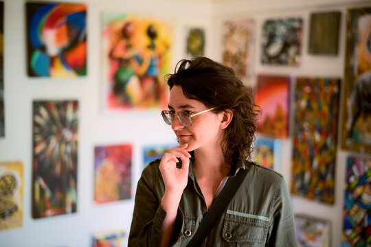 Young woman smiling intrigued in a gallery surrounded by colorful abstract paintings on the walls. Kigali, Rwanda