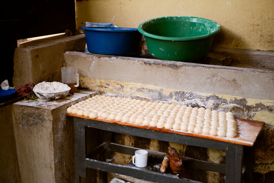 Dough balls arranged on a wooden table in a rustic kitchen with bowls and flour nearby. Kigali, Rwanda