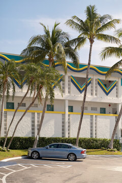 Vintage hotel facade with palm trees and a parked silver car in a sunny tropical setting. Miami, Florida, USA