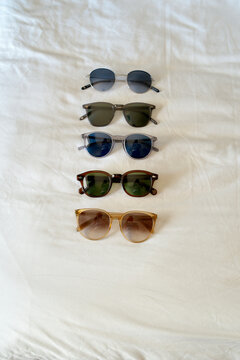 Five pairs of sunglasses neatly arranged on a white sheet in a vertical line. Miami, Florida, USA