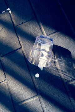 Spilled milk from a plastic cup on a textured dark pavement under sunlight and shadow. Miami, Florida, USA