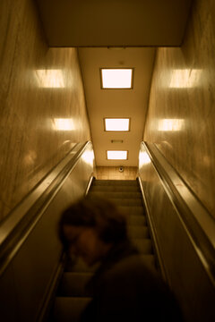 Dimly lit escalator with blurred person descending under square ceiling lights. Belgium