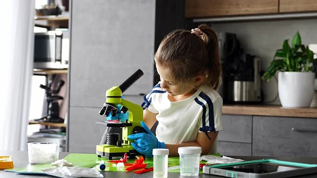 Young girl studying crystal structure through microscope during home science experiment with growing crystals kit. Early STEM education and curiosity driven scientific exploration at home.