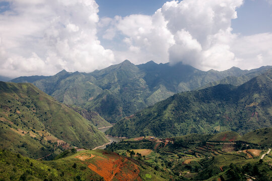 Lush green mountains under a cloudy sky with terraced fields and river valley. Mountains of Ta Xua, Bac Yen District, Son La, Vietnam