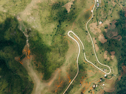 Aerial view of a winding road through a lush, green mountainous landscape with scattered houses. Ta Xua, Bac Yen District, Son La, Vietnam