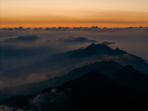 Mountain peaks at sunset under a sky with orange and blue hues with layers of mist. Ta Xua, Bac Yen District, Son La, Vietnam