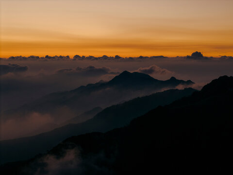 Silhouetted mountain range at sunset with misty clouds and an orange sky. Ta Xua, Bac Yen District, Son La, Vietnam