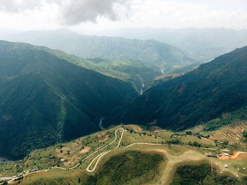 Aerial view of winding road through lush green mountains under a cloudy sky.   Ta Xua, Bac Yen District, Son La, Vietnam