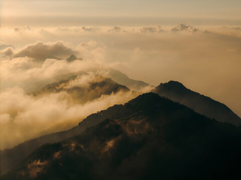 Majestic mountain peaks surrounded by golden clouds under a soft, morning light. Ta Xua, Bac Yen District, Son La, Vietnam
