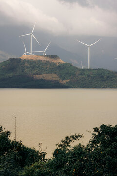 Wind turbines on a hilltop overlooking a serene lake under a cloudy sky. Huong Hoa, Quang Tri, Vietnam