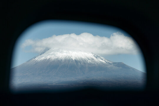 Snow-capped mountain peak viewed through a car window with clouds above against blue sky. Mount Fuji, Japan